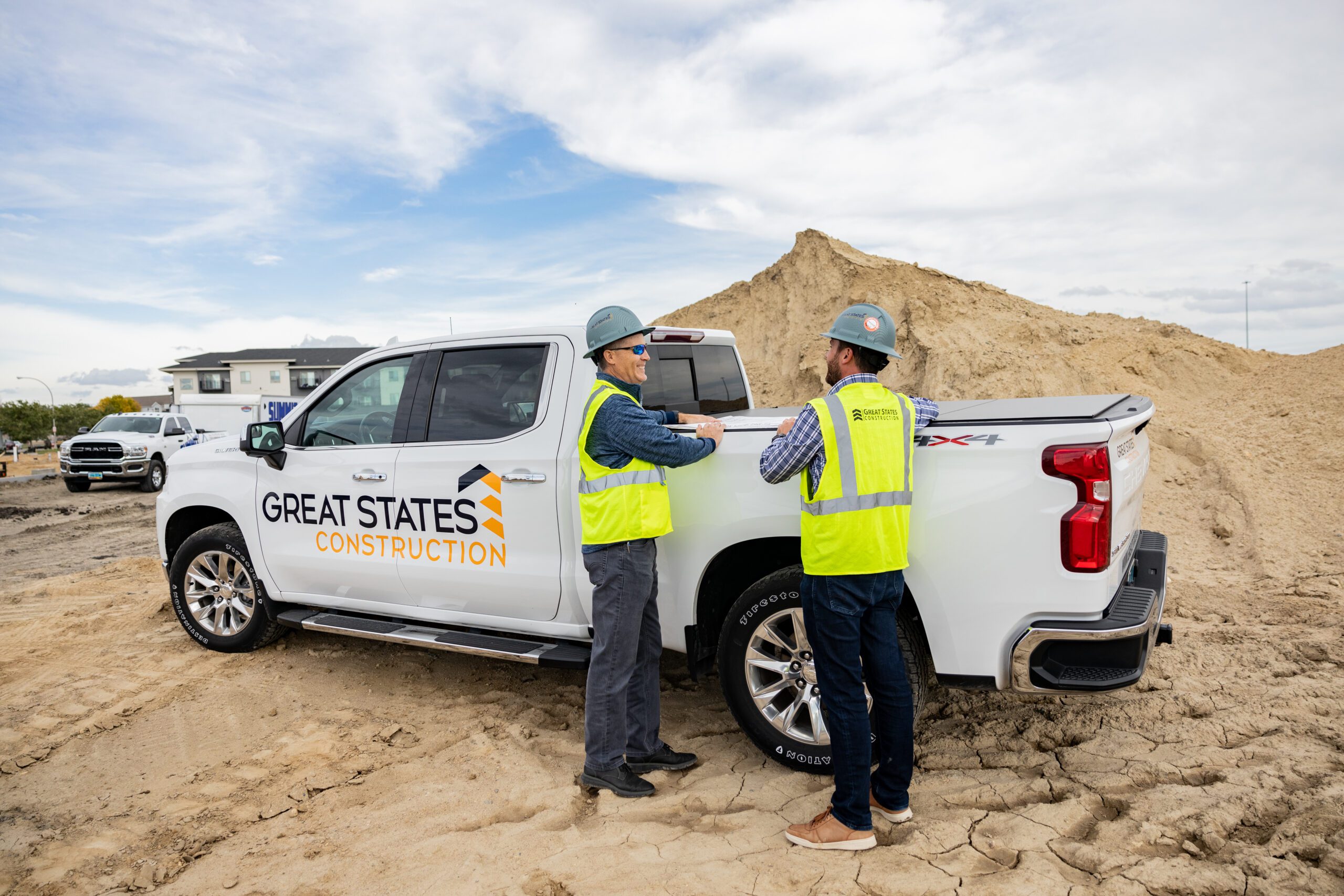 Great States Construction general contractor team members in hard hats reviewing plans beside company truck at active construction site in Fargo, North Dakota