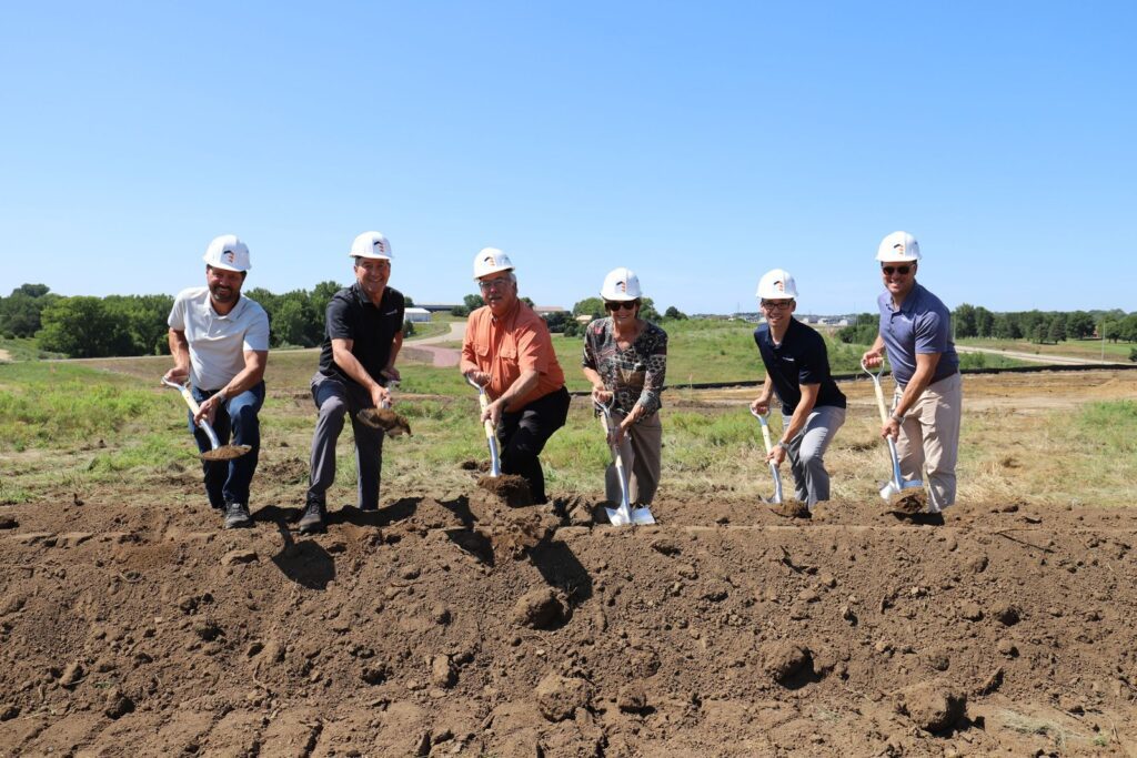 Six people in Great States Construction hard hats turning dirt with shovels at the Emra Sioux Falls groundbreaking